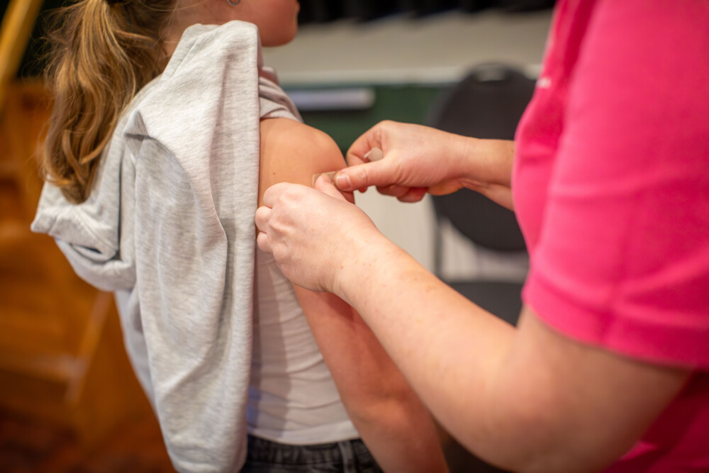 Meisje krijgt pleister op haar arm geplakt nadat zij gevaccineerd is door een medewerker van de GGD